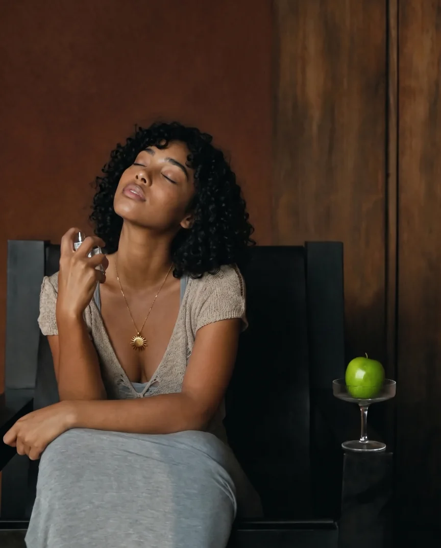 A seated person sprays perfume with a green apple nearby.