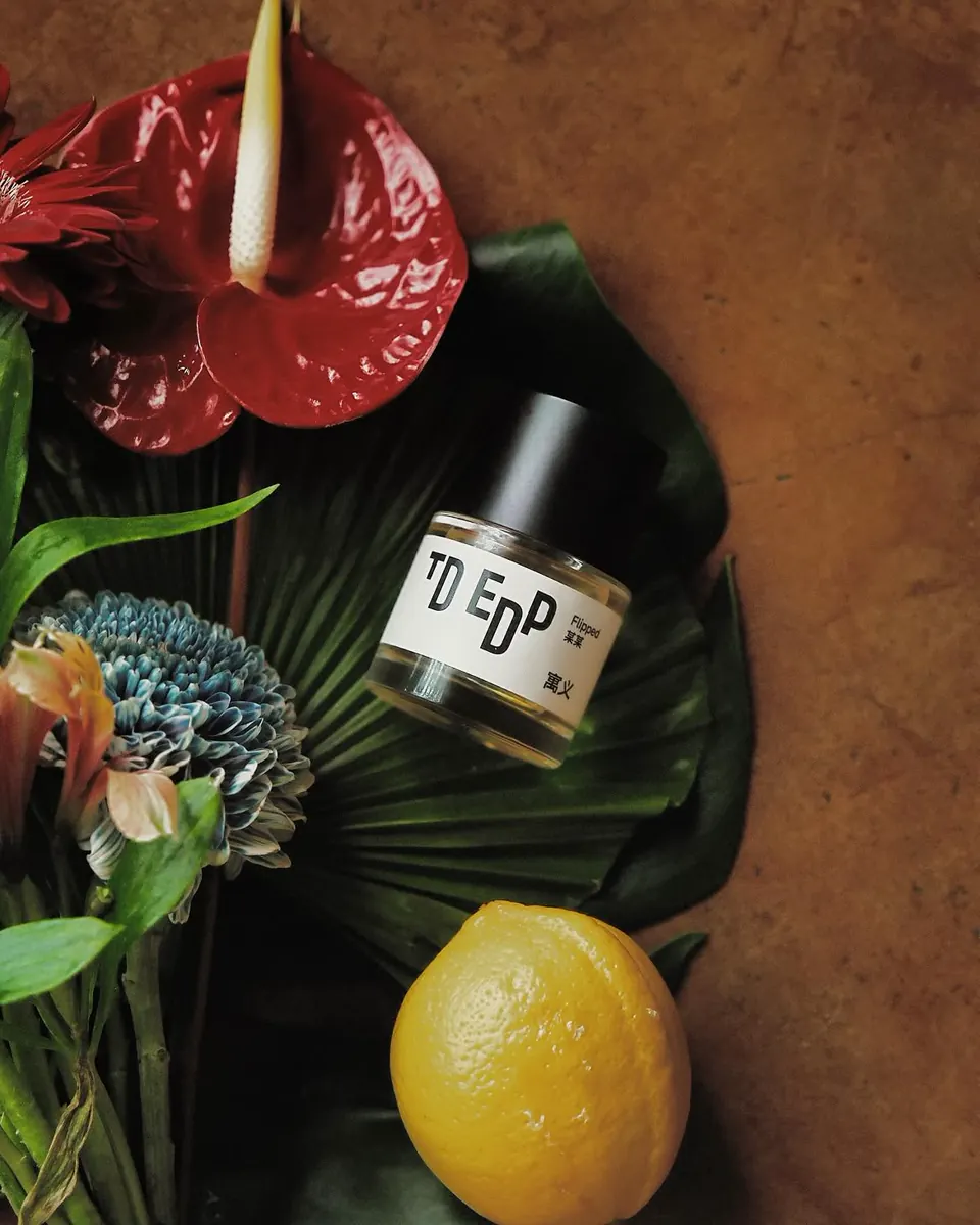 Perfume bottle with vivid flowers, leaves and lemon; a product-only scene.