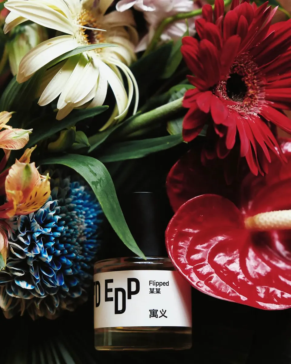 Perfume bottle among red, white and blue flowers; no person in frame.